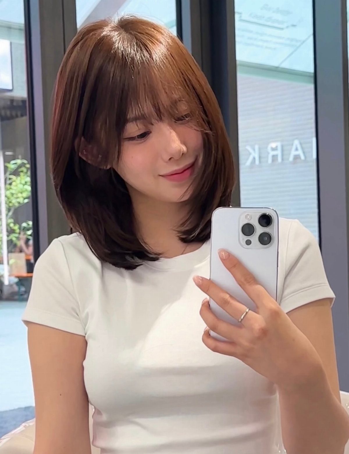 Woman with medium brown layered hair and bangs takes a mirror selfie