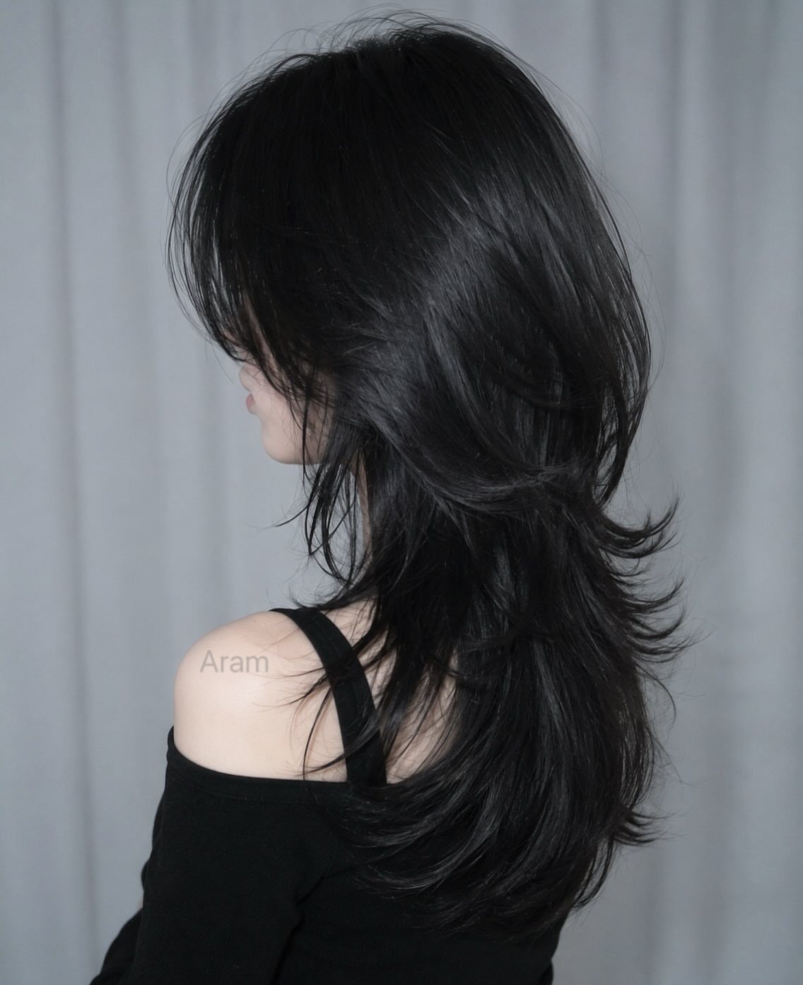 Side profile showing long black wolf cut with wispy bangs and feathered layers