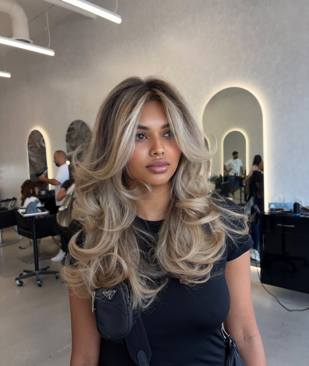 Woman displaying voluminous blonde layers with bouncy, curled ends in a salon