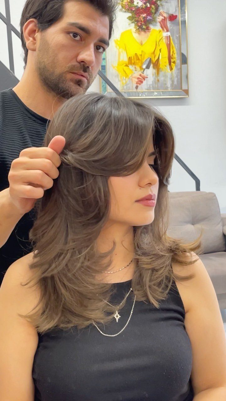 Woman displaying medium-length brown layers with center-parted curtain bangs in a salon