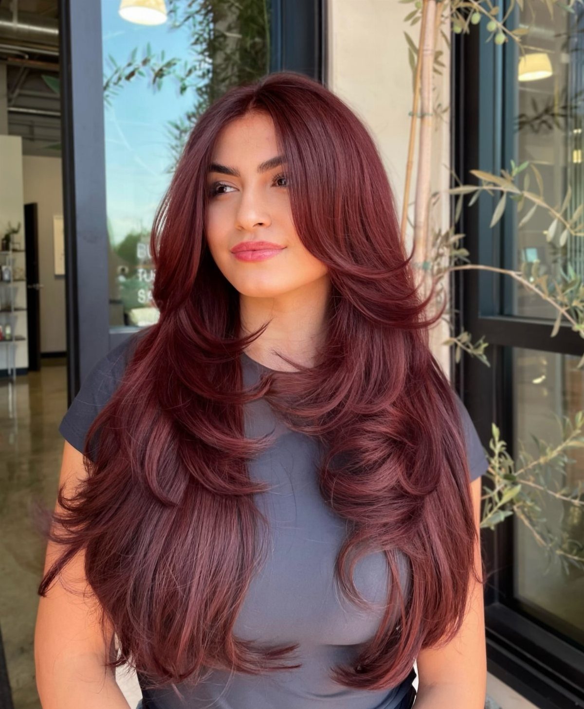 Woman with long burgundy waterfall layers and curled, turned ends