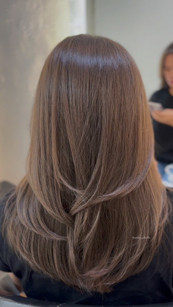 Long ash-brown hair falls in smooth layers down a salon client’s back