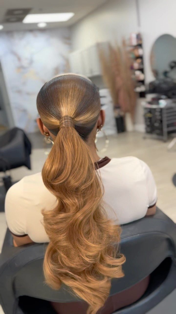 Glossy dark-rooted caramel ponytail cascading in loose curls in a salon
