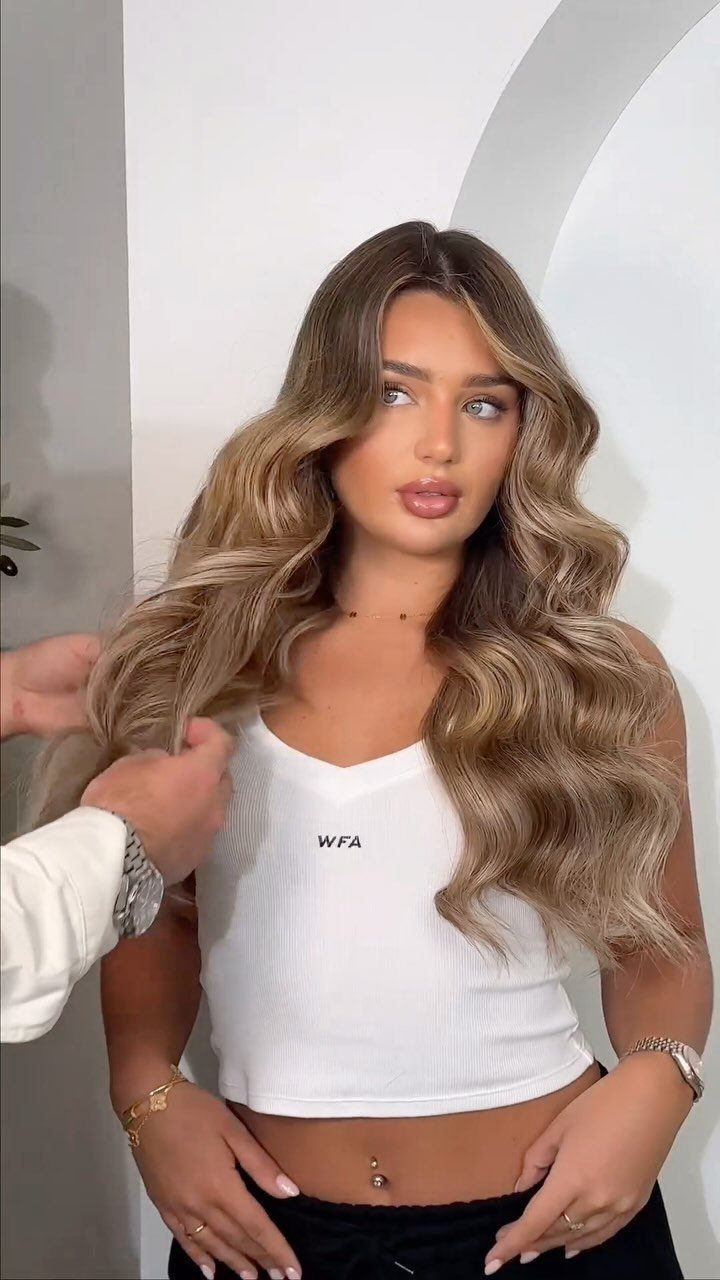 Woman with highlighted light brown waves as a stylist adjusts her hair