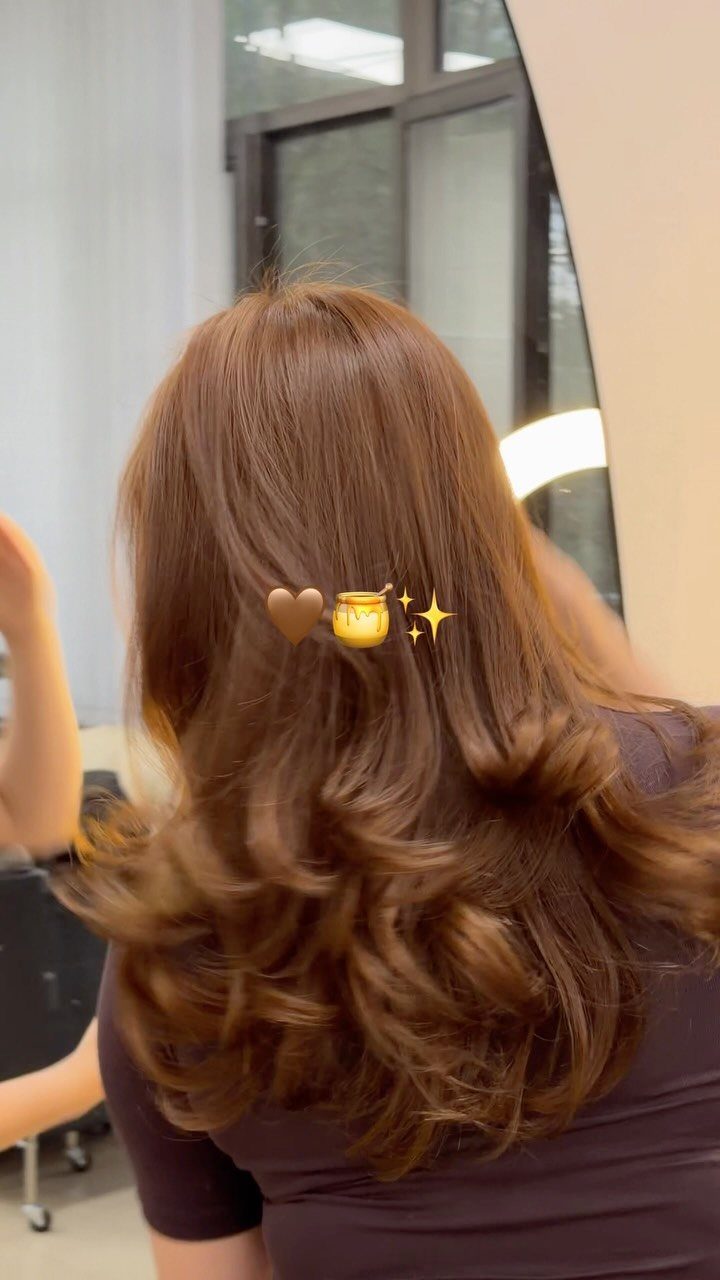 Long warm brown hair falls in glossy loose curls over a dark purple top.