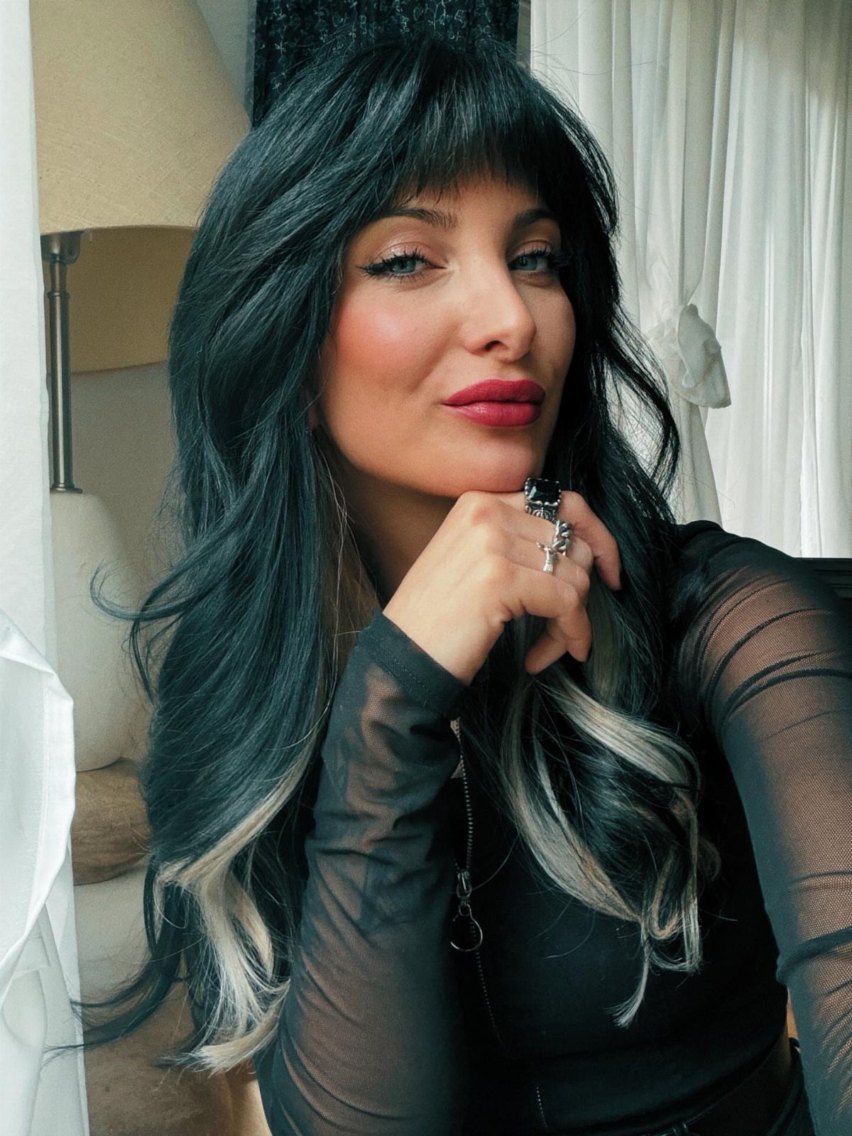 Woman with long dark waves, blunt bangs, and pale streaks at the ends