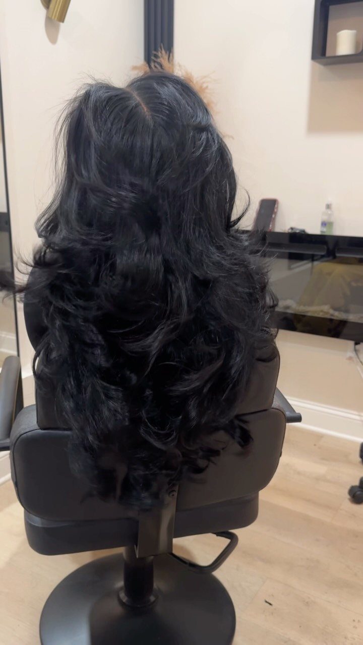 Long black layered hair falls in glossy, voluminous curls down the back.