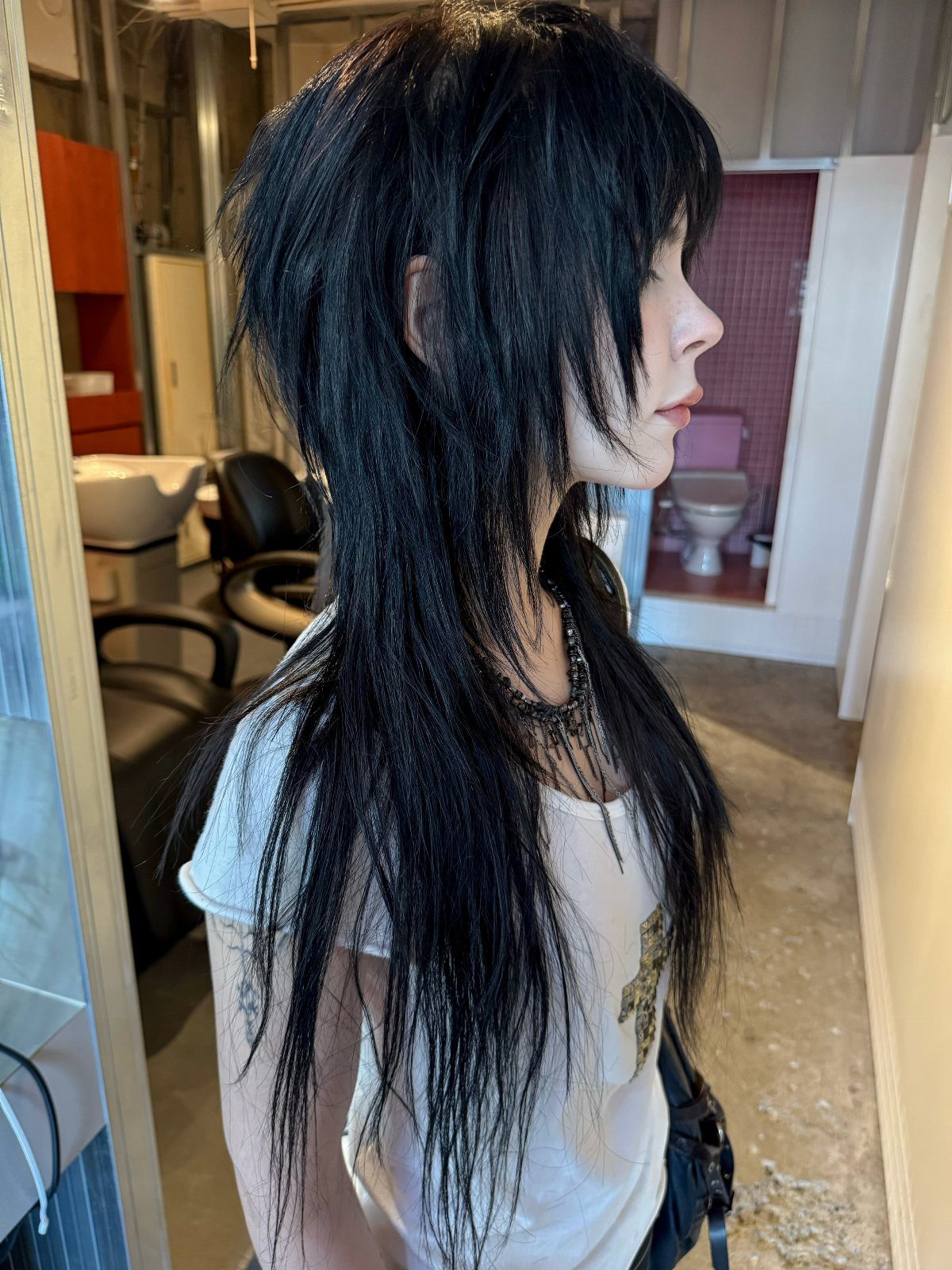 Long layered black hair with heavy bangs shown in profile at a salon