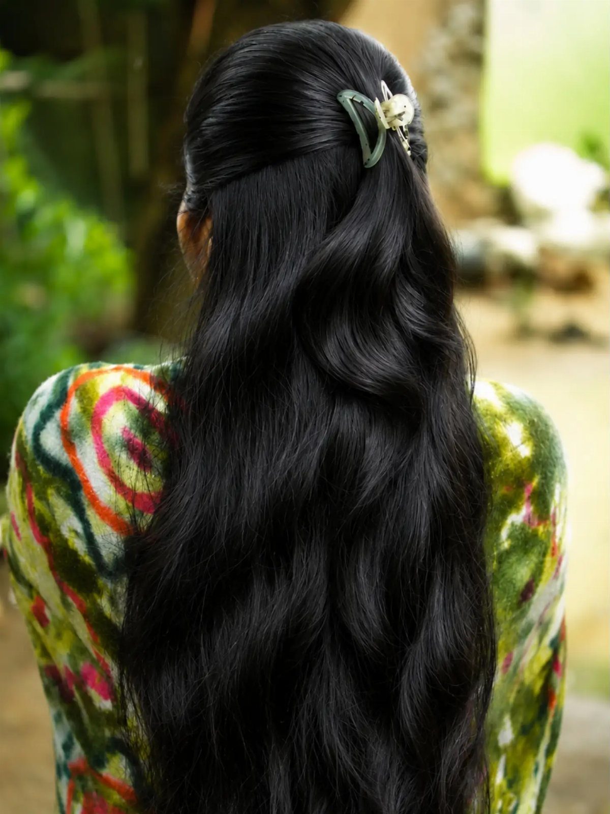 Long black hair falls loose beneath a pale green butterfly clip