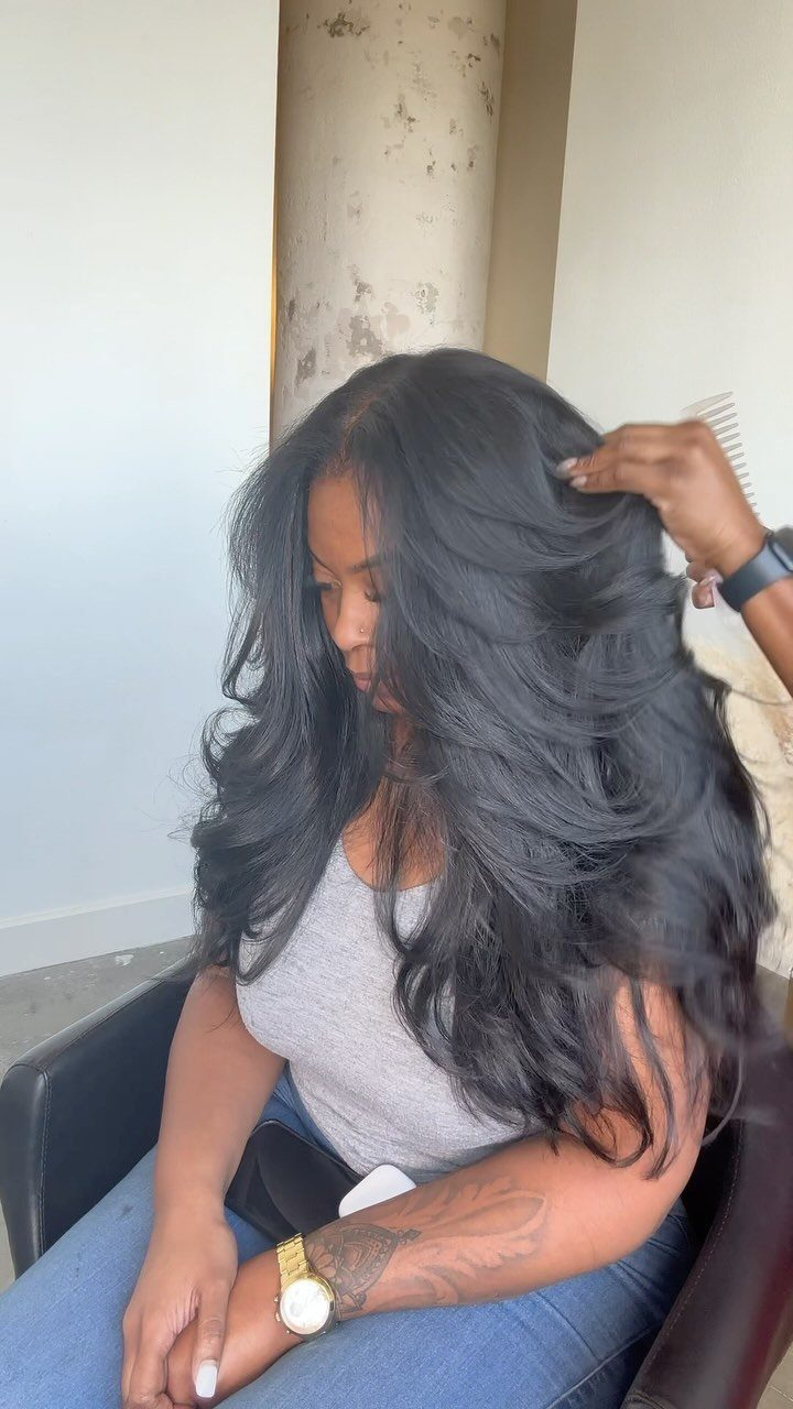 Long glossy black waves fall over a seated woman as she adjusts her hair