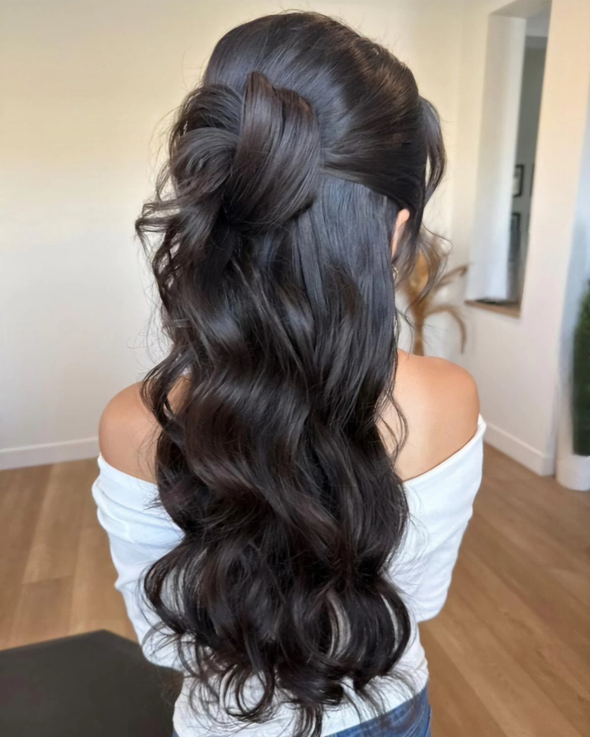 Long black hair styled in loose waves with a twisted half-updo