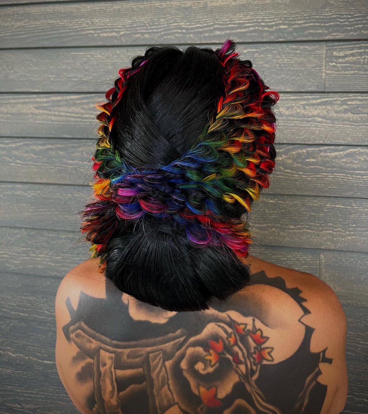Rainbow-wrapped black updo with colorful strands against a gray wooden wall