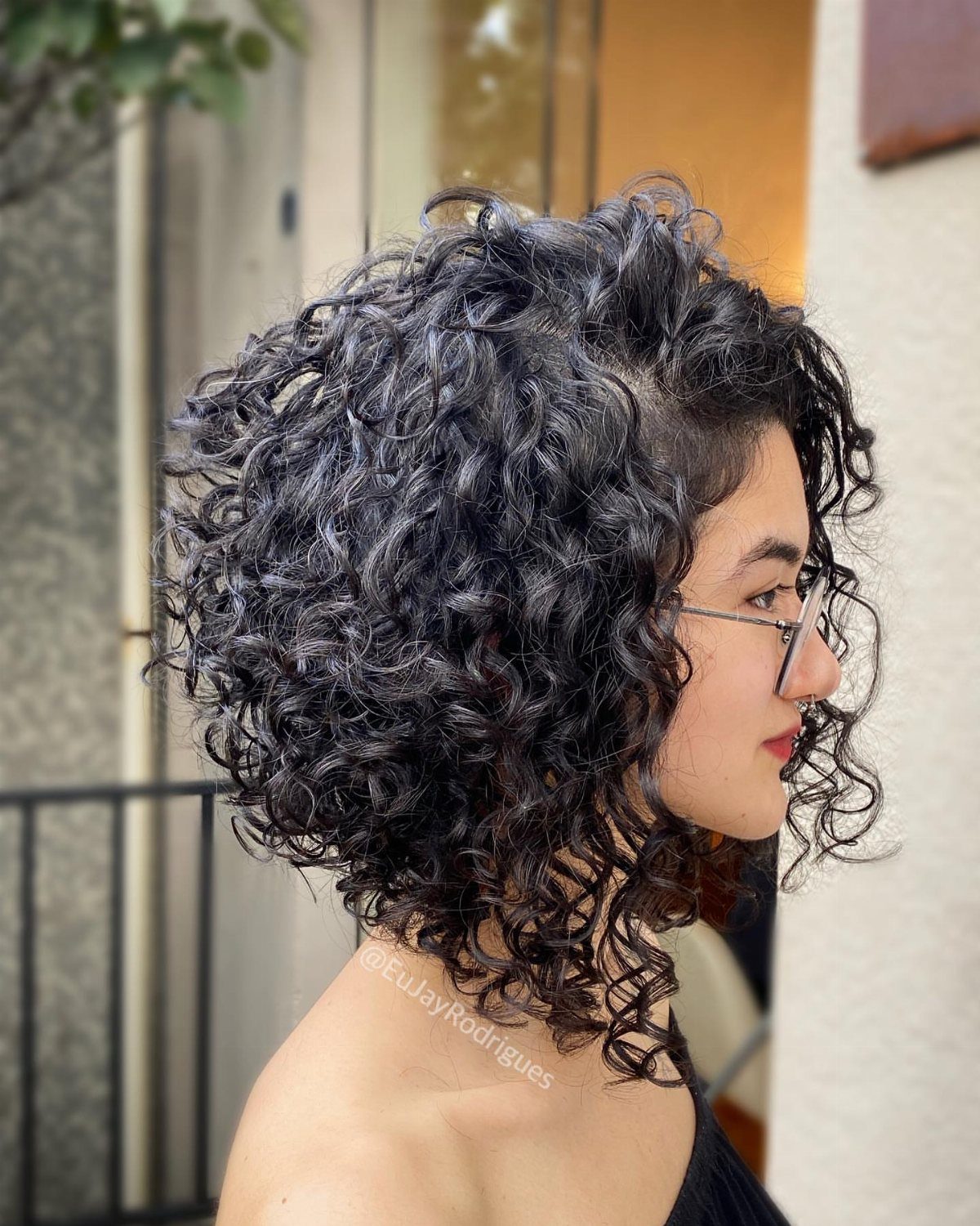 Woman with shoulder-length layered dark curls posing in profile indoors