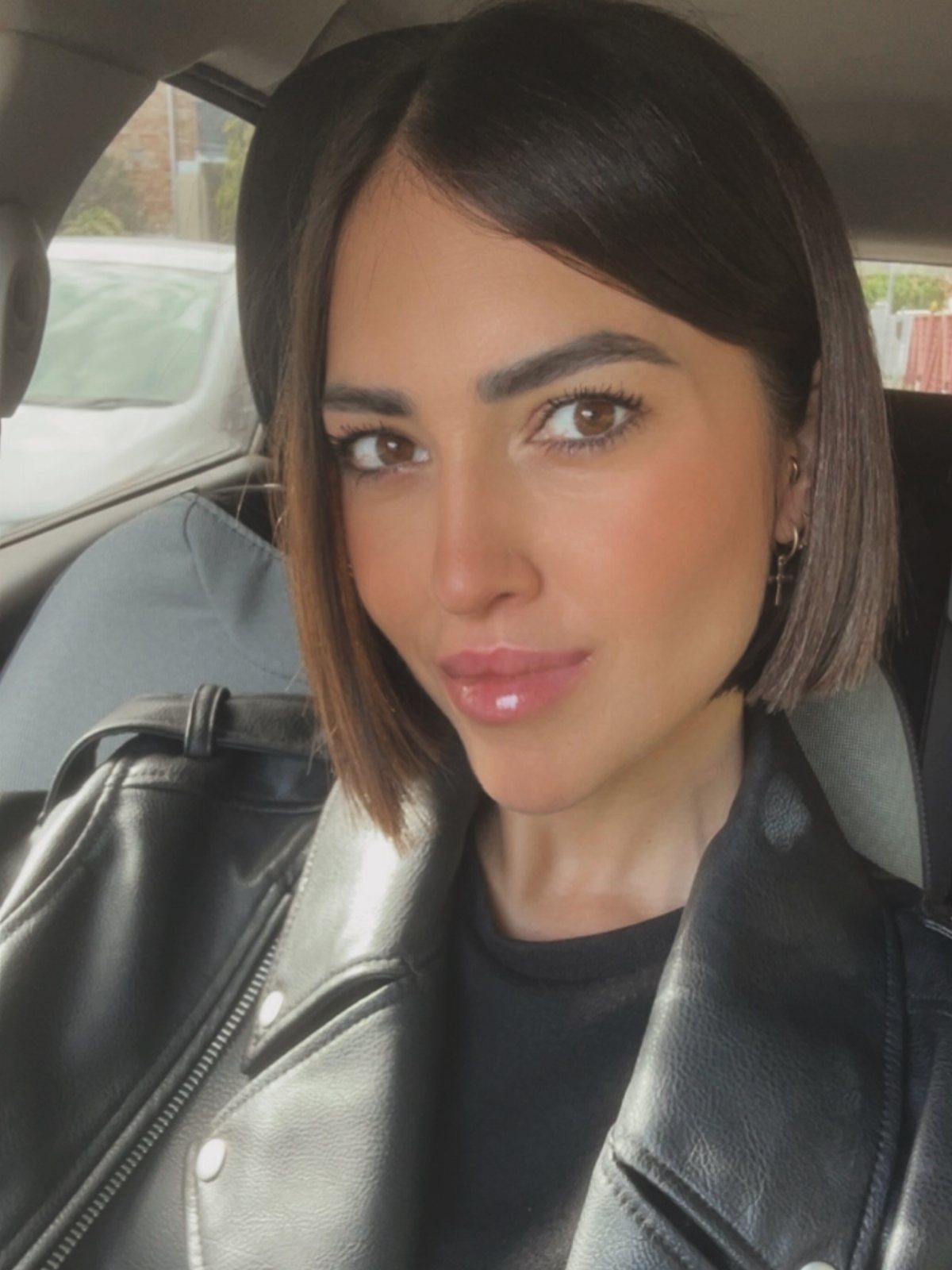 Woman posing in a car with a sleek, side-parted chin-length dark bob