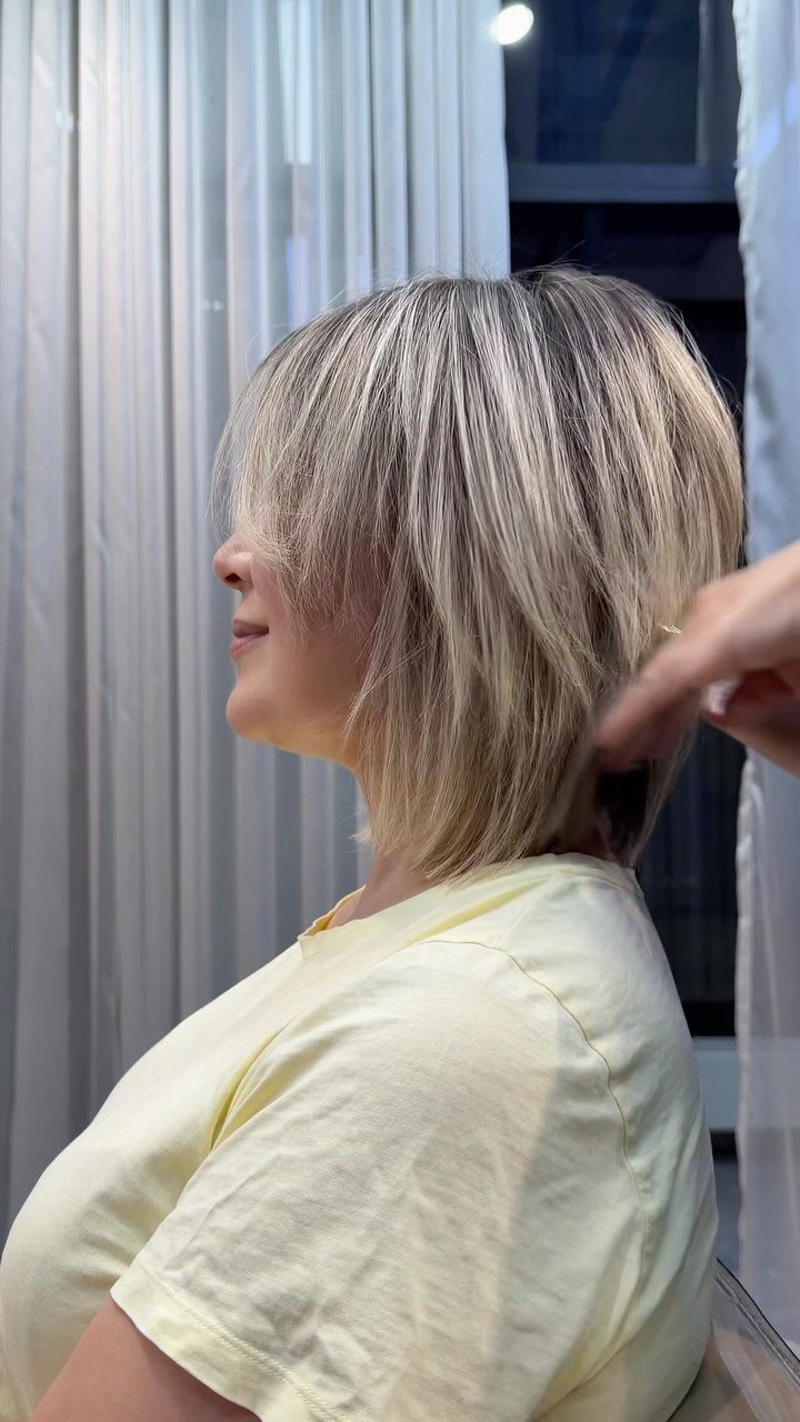 Wispy layered blonde lob with feathered ends and long fringe in a salon