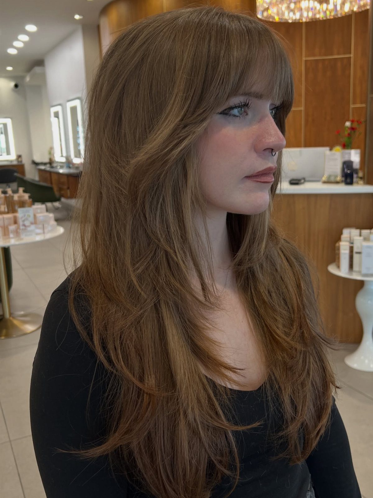 Woman with long caramel-brown layered waves and full bangs in a salon