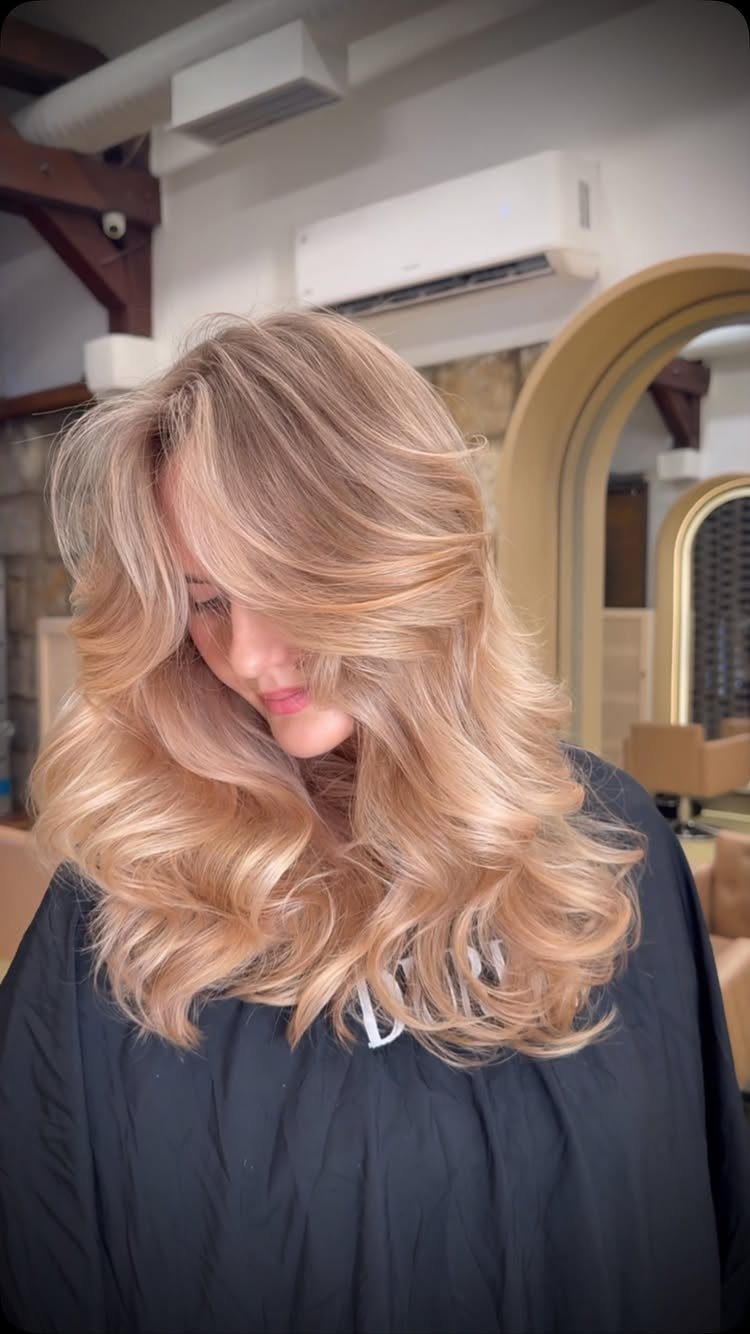 Long honey-blonde layered hair styled in loose, voluminous waves in a salon.