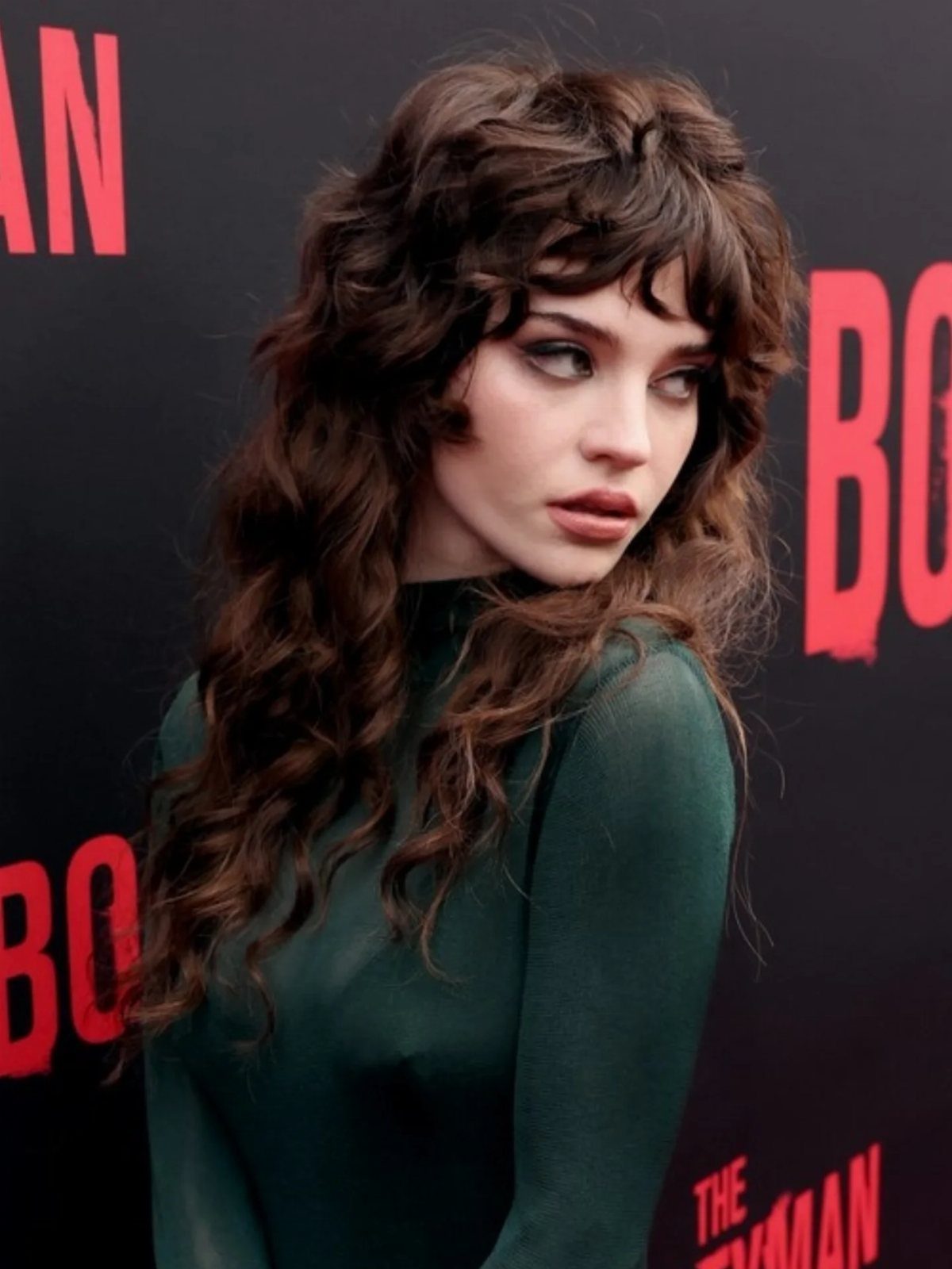 Woman with wispy fringe and long, layered dark waves poses before a black backdrop