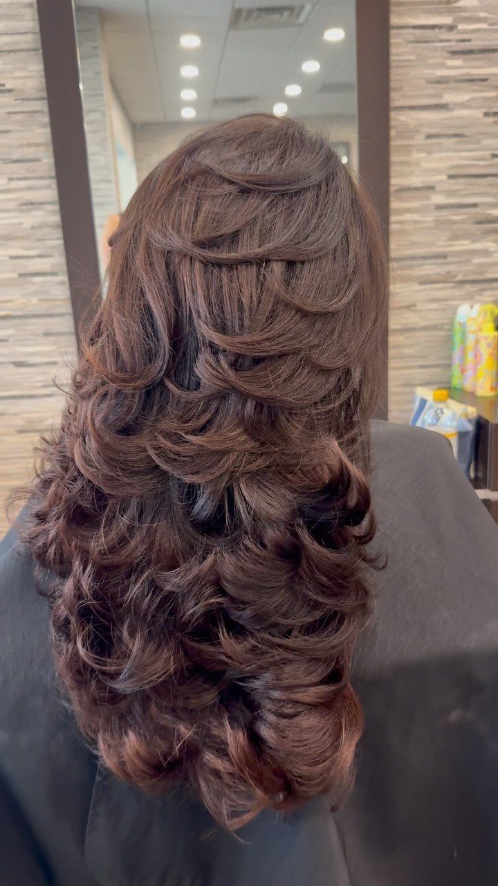 Long brown hair styled in loose, voluminous curls and cascading layers
