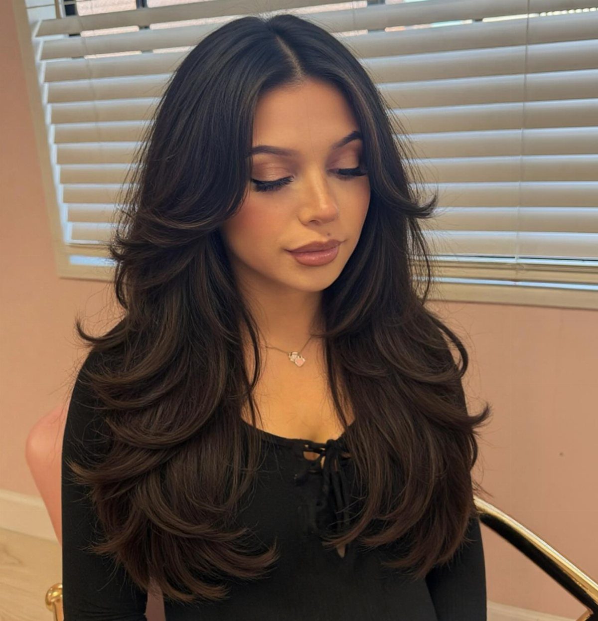 Long dark hair falls in voluminous S-shaped layers around a woman's shoulders