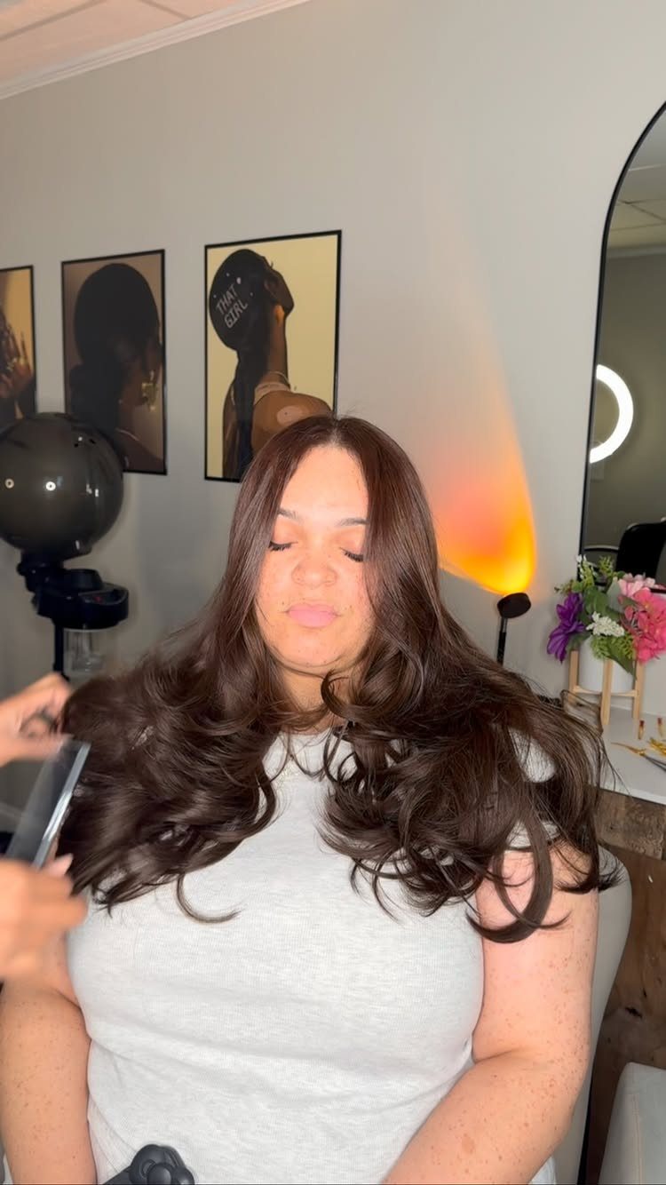 Woman with long dark layered hair styled in loose, smooth waves