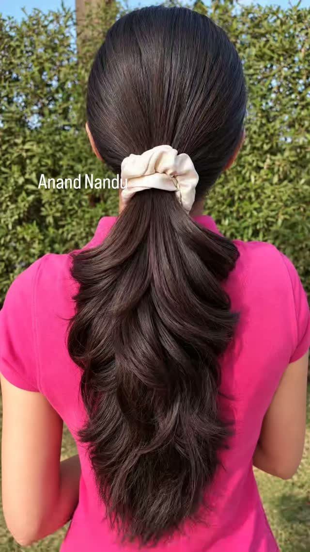 Long dark layered hair falls in soft curls below a cream scrunchie