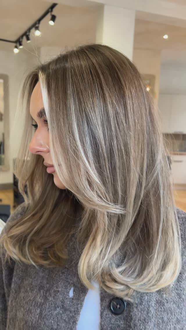 Long layered ash-brown hair with pale blonde highlights in a salon