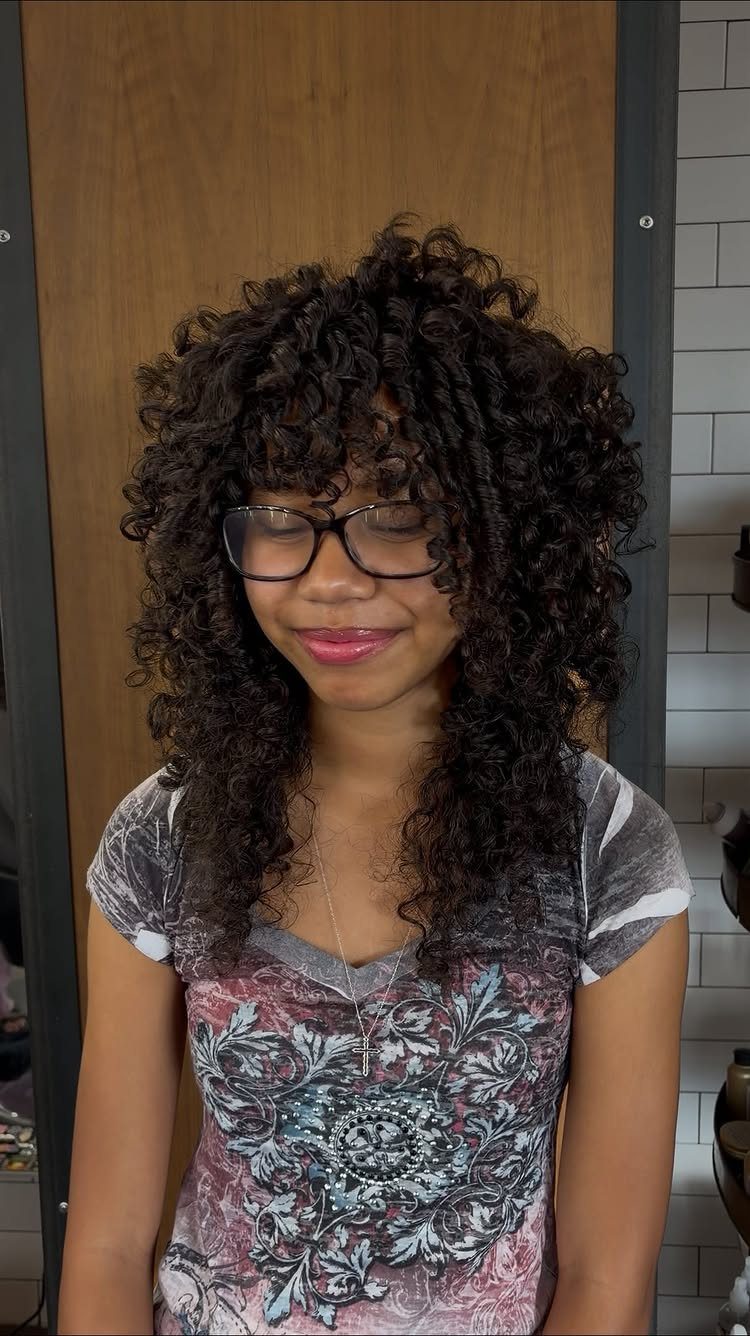 Long layered curls frame a person’s face as they pose in glasses