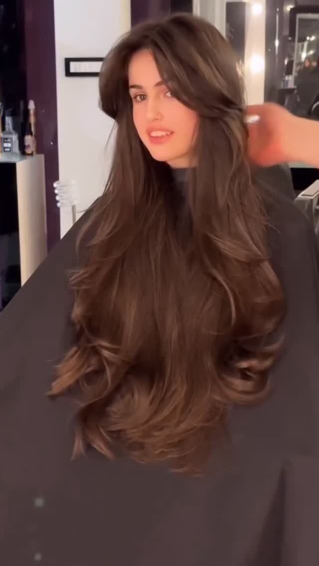 Long brown layered hair falls in soft curls over a salon cape