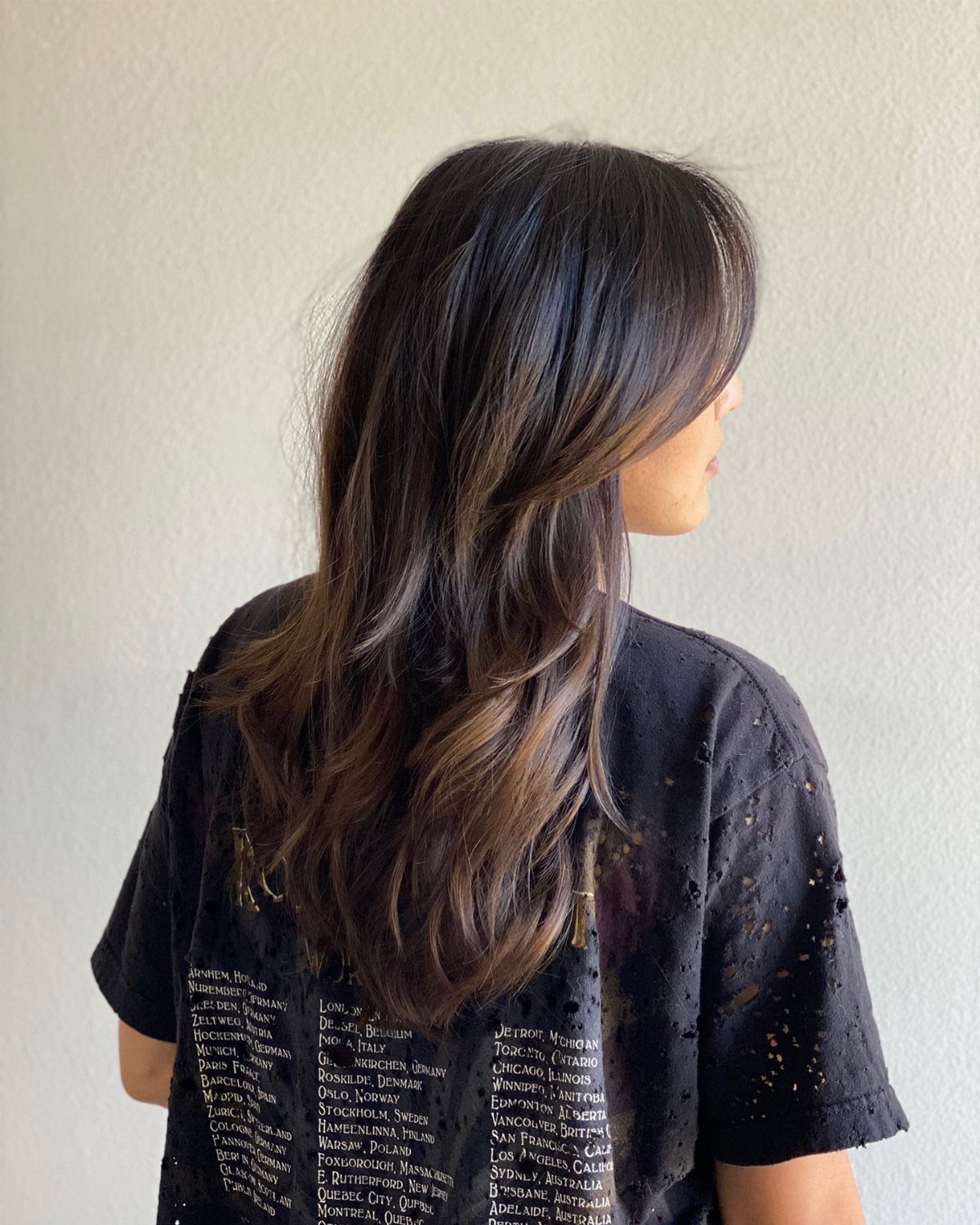 Long dark layered hair with side-swept bangs shown from behind