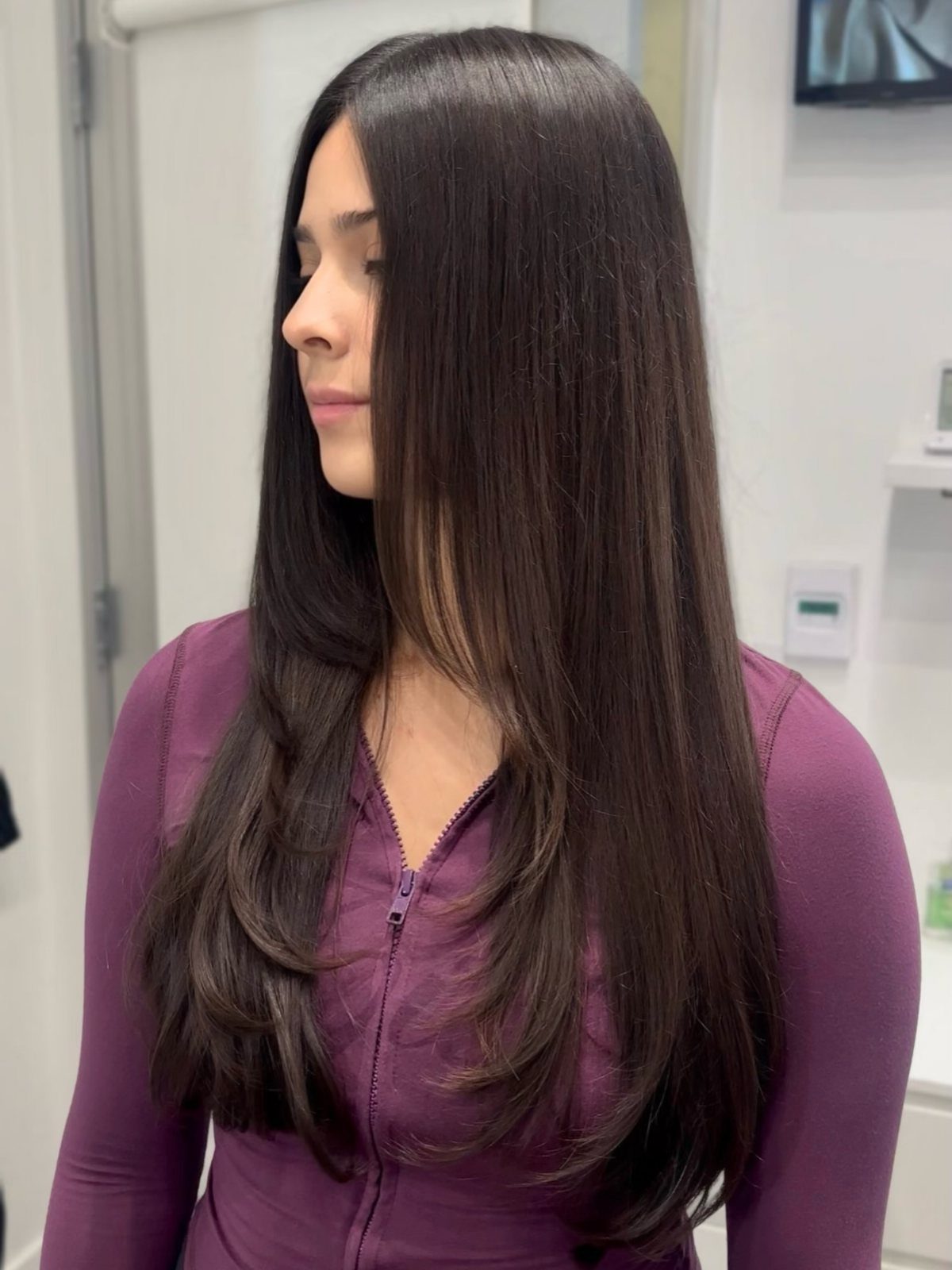 Long straight layered hair falls smoothly over a purple top