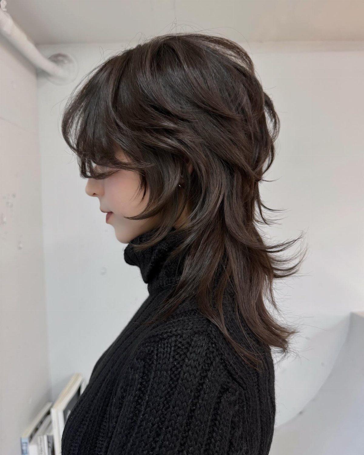 Dark layered hair with wispy bangs and feathered ends, shown in profile