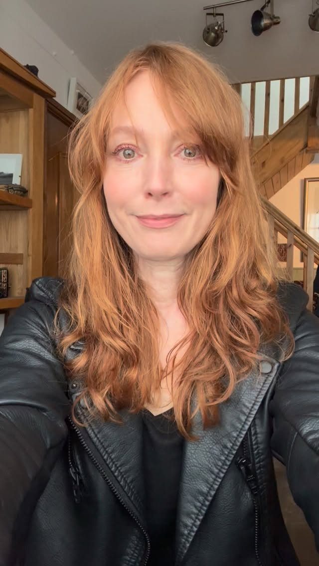 Woman with long, wavy strawberry-blonde hair posing in a black leather jacket