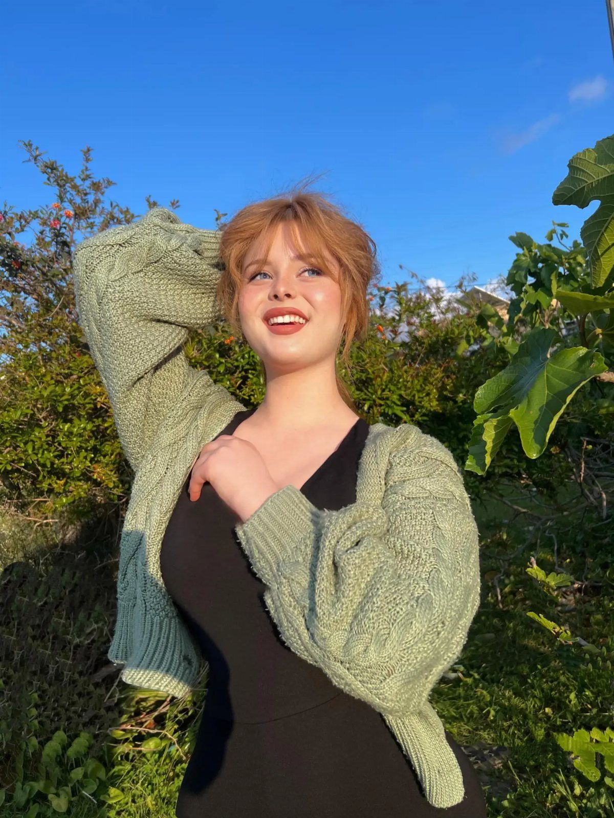 Young woman with reddish hair poses in a pale green knit cardigan outdoors