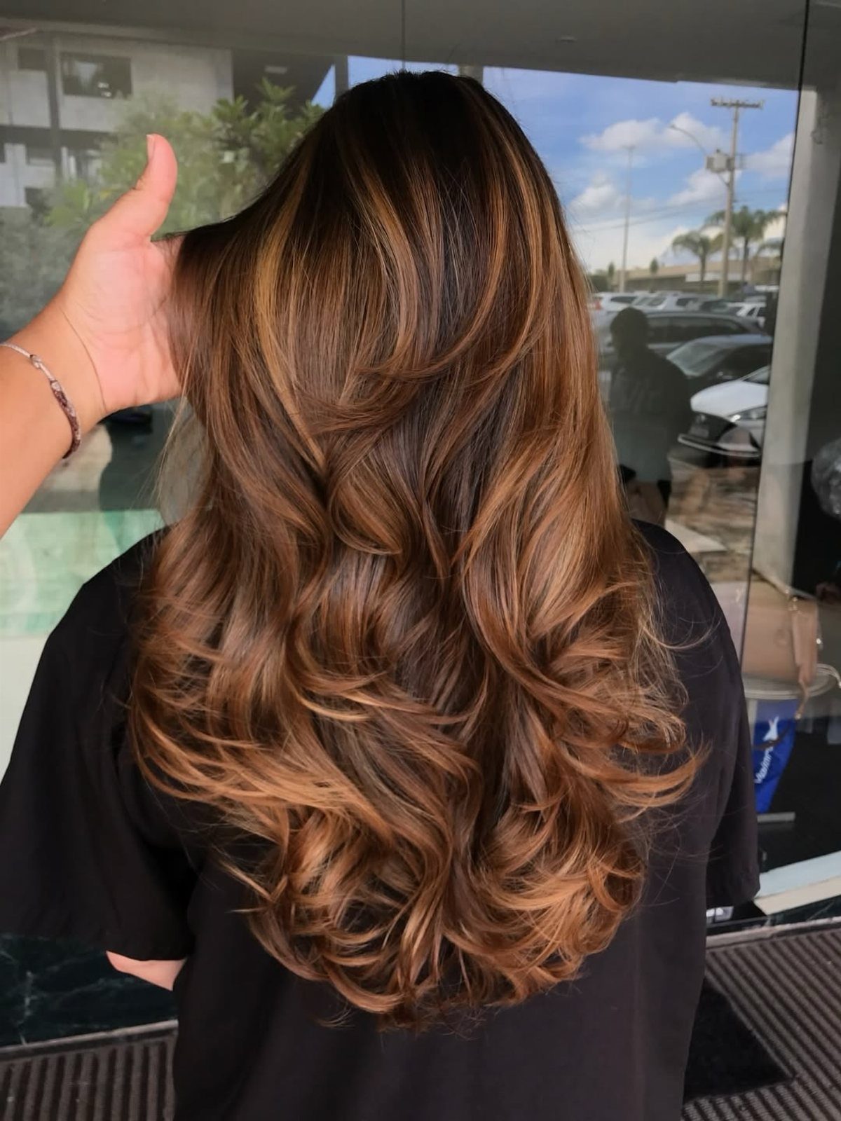Long wavy chestnut-brown hair fading from dark roots into warm curled ends