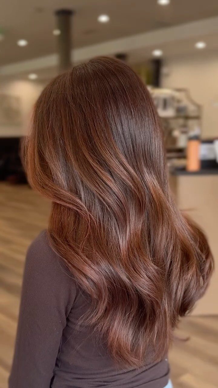 Long glossy auburn-brown hair falls in soft waves down a salon client’s back