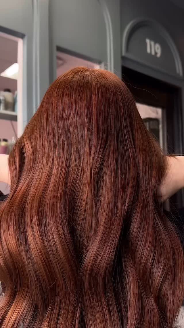 Long wavy copper auburn hair with glossy reddish highlights in a salon