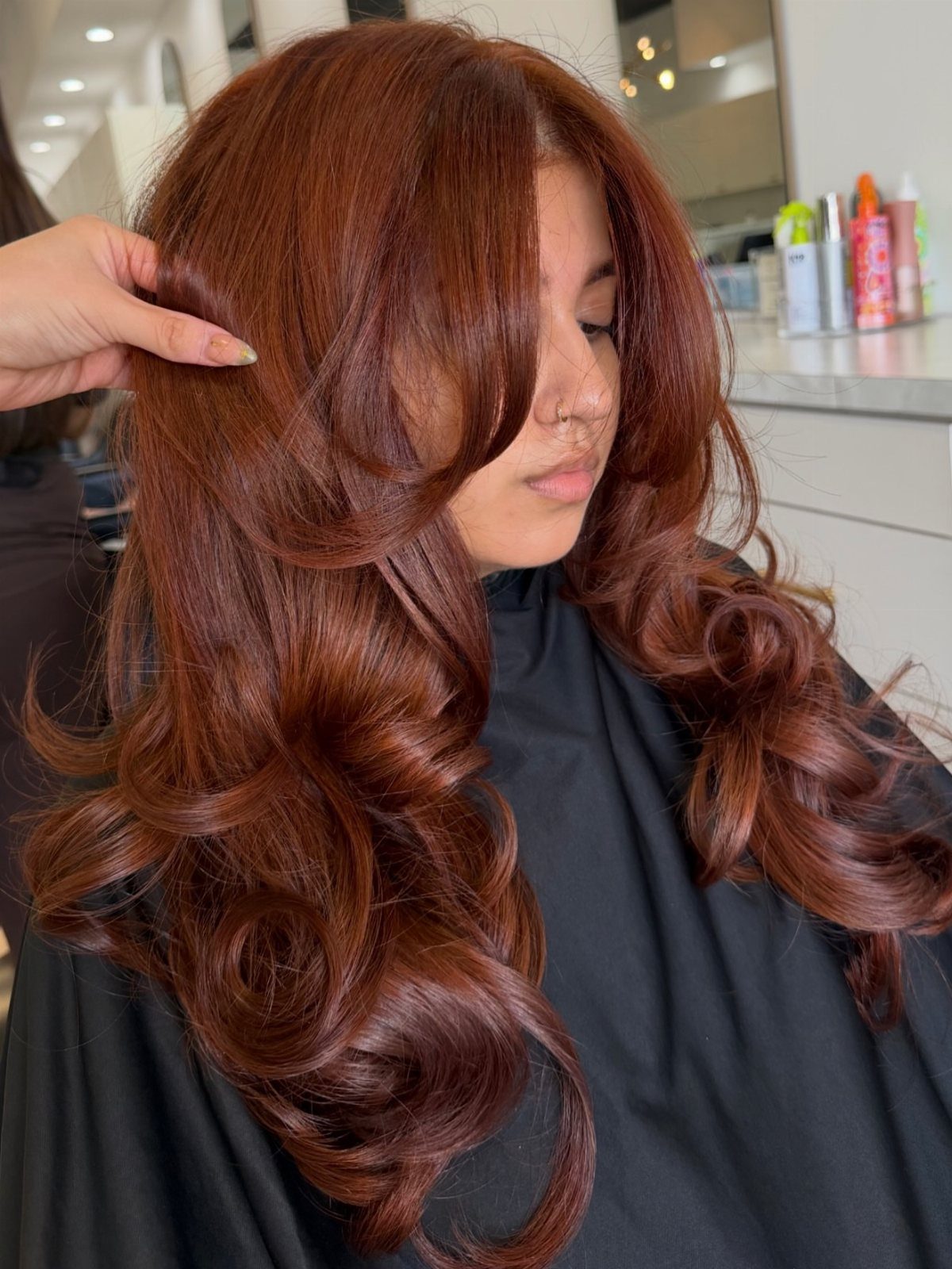 Long reddish-brown layered curls styled on a woman in a salon