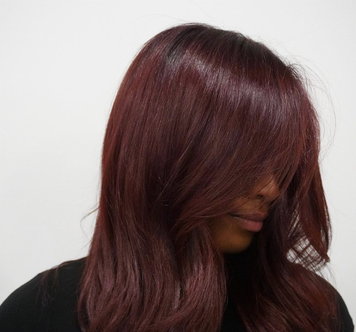 Long layered hair in a deep, glossy red-brown shade frames a partially obscured face.