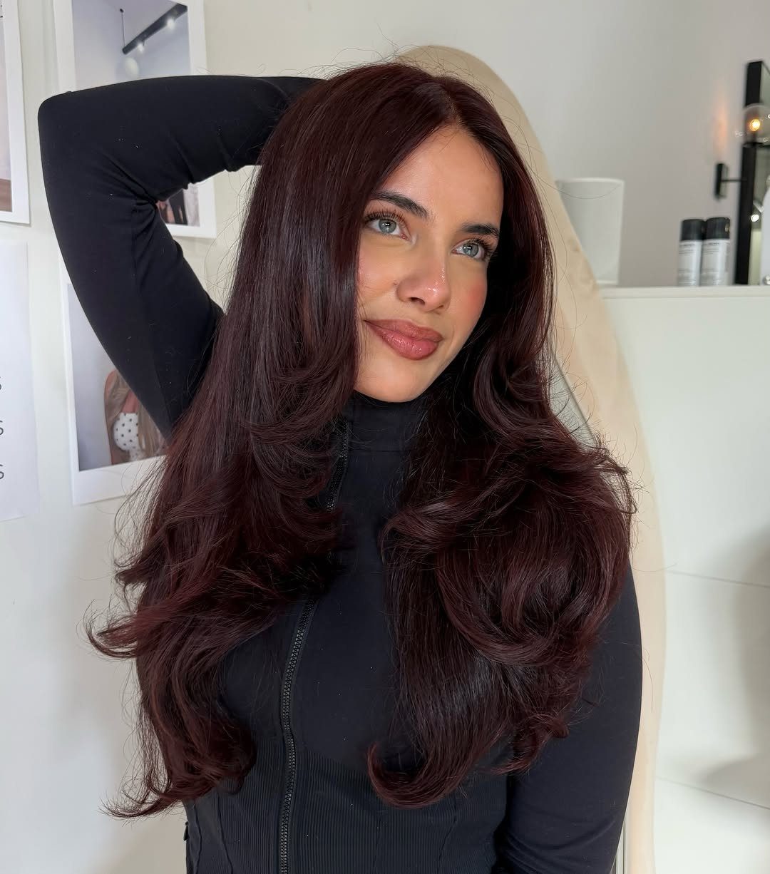 Woman with long, voluminous dark burgundy hair posing in a bright salon