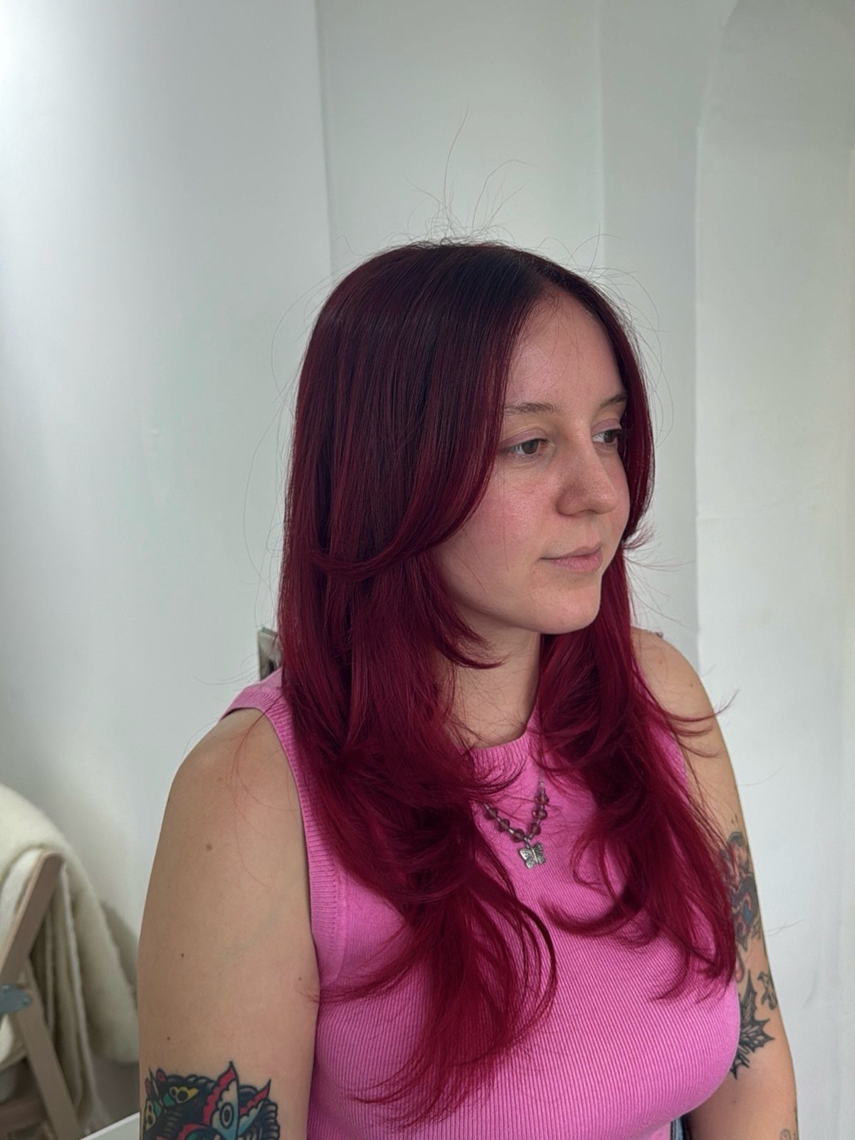 Woman with long, wavy deep red hair wearing a pink sleeveless top