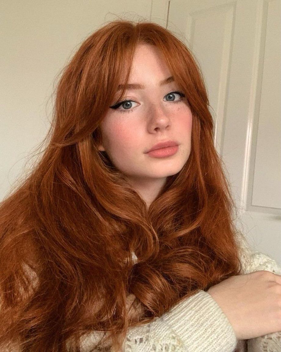 Young woman with long, wavy ginger hair and curtain bangs