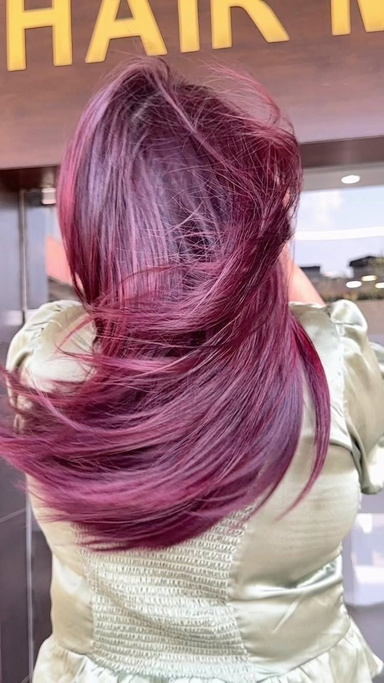 Long glossy plum-red hair flowing down a person’s back in a salon