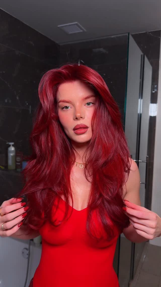 Woman showing long, vivid ruby-red hair in a dark tiled bathroom
