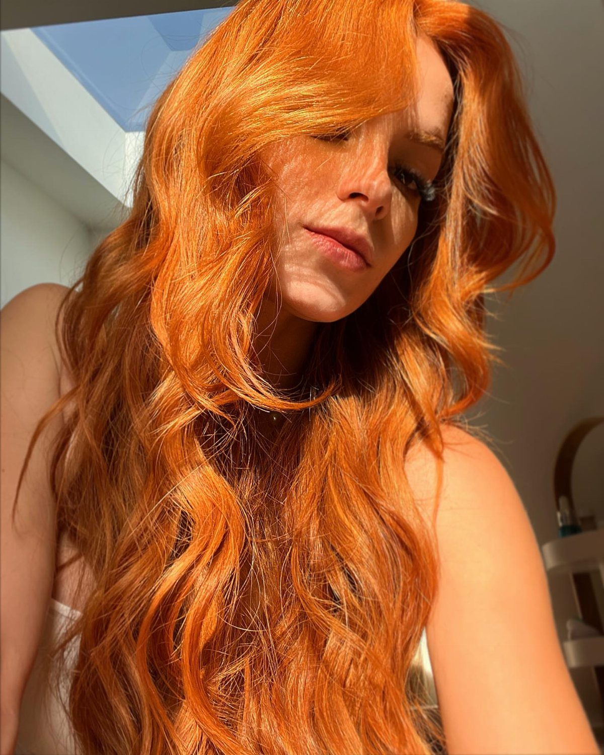 Woman with long, wavy blood-orange hair in bright natural sunlight