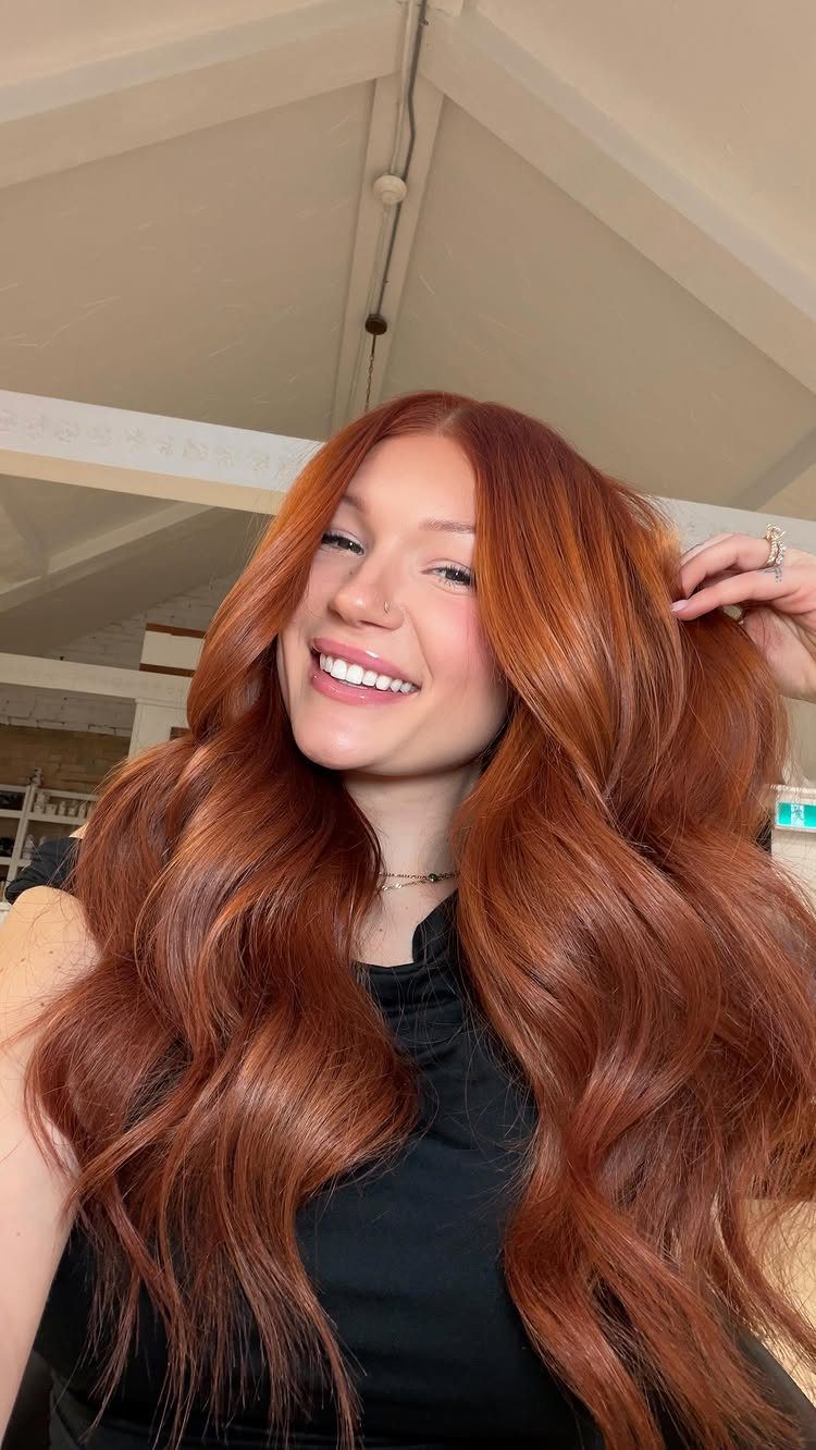 Woman with long, wavy copper-red hair posing indoors in a black top