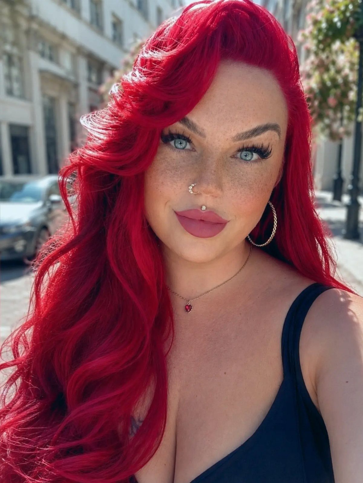 Woman with long, vivid crimson-red hair posing on a city sidewalk