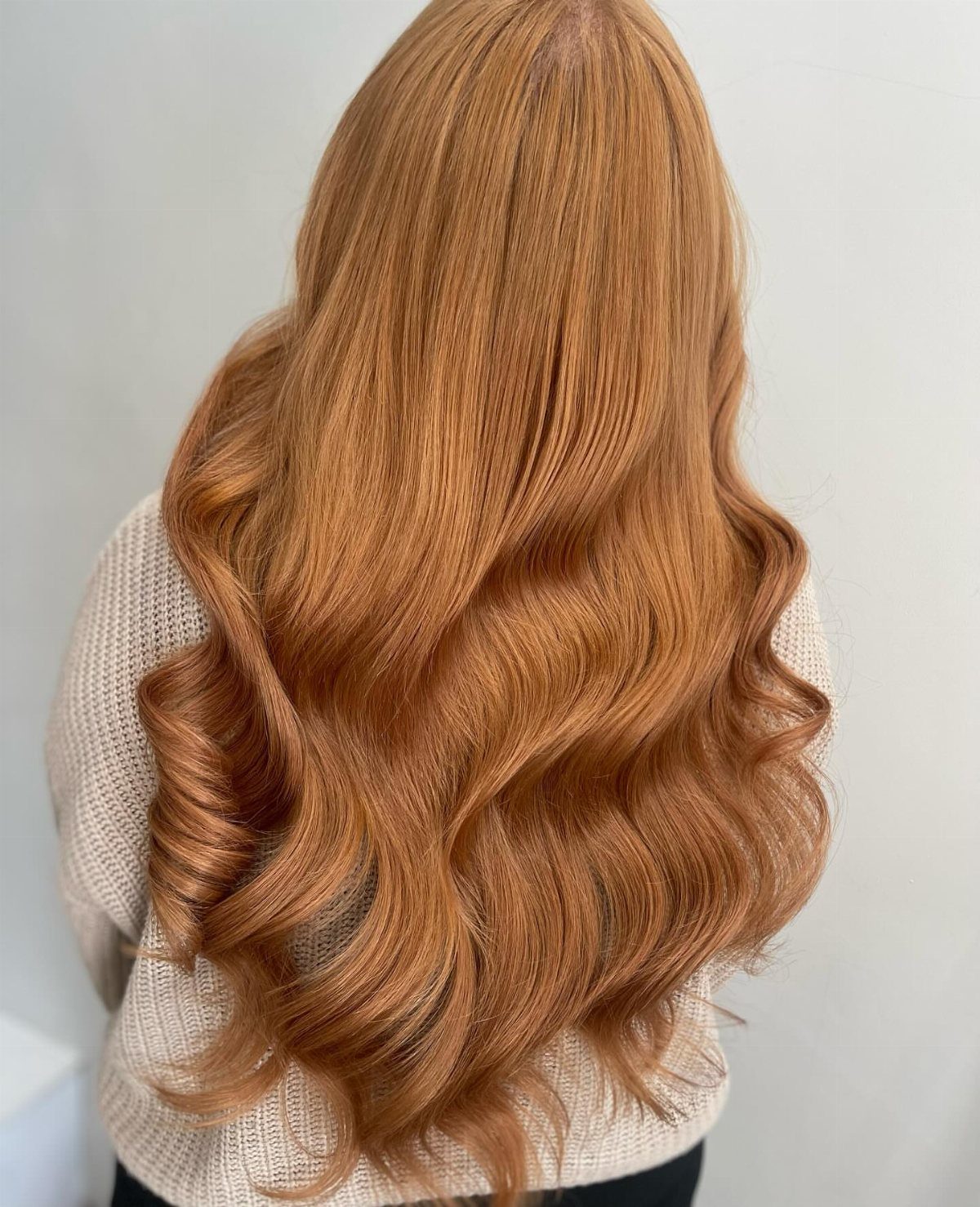 Long strawberry-blonde hair with loose waves over a cream knit sweater