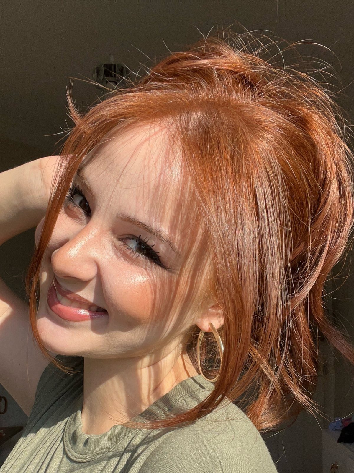 Woman smiles in sunlight, showing long natural-looking light auburn hair