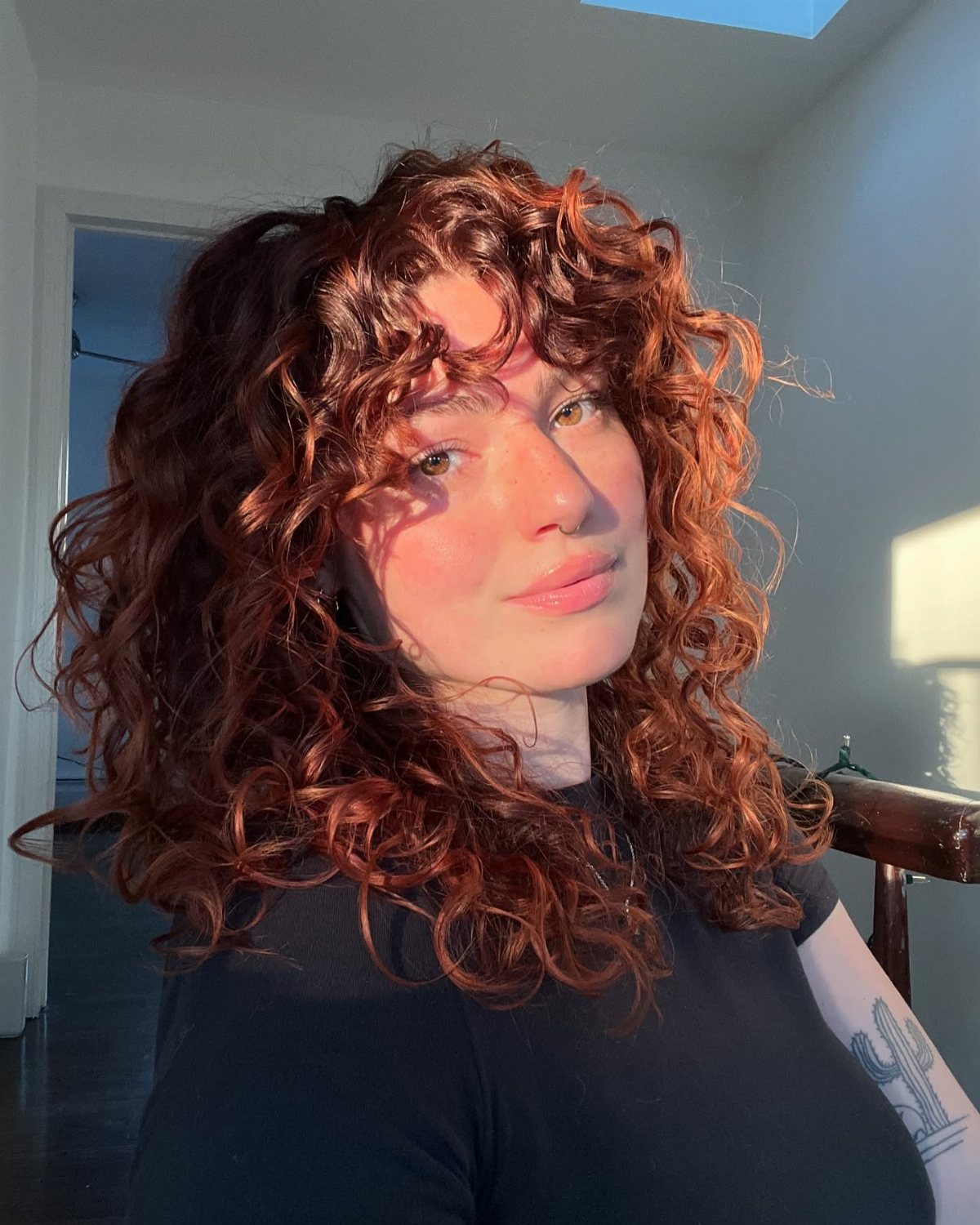 Person posing with long, curly reddish-brown hair in bright sunlight
